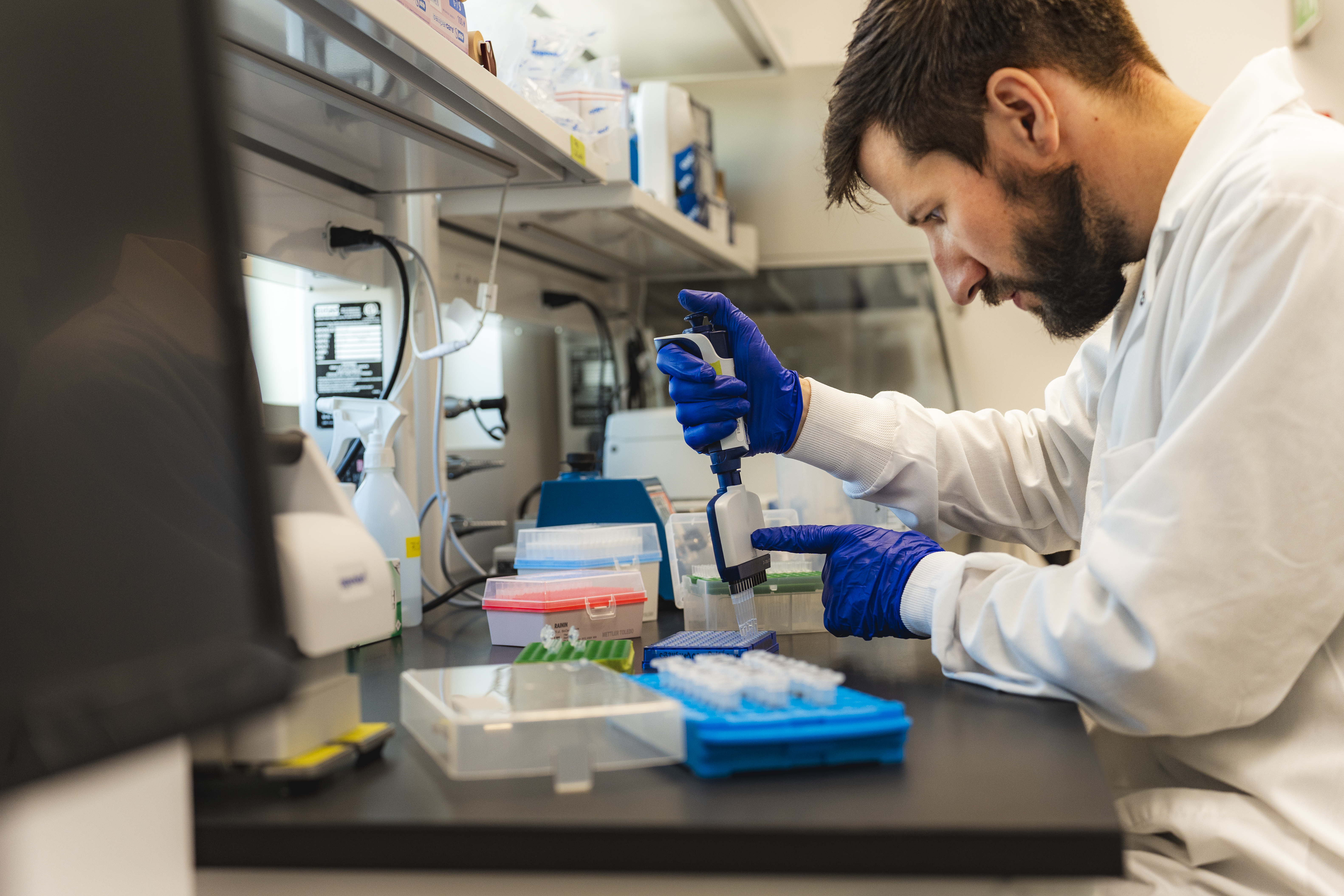 A man in a lab coat, injecting something into small test tubes.